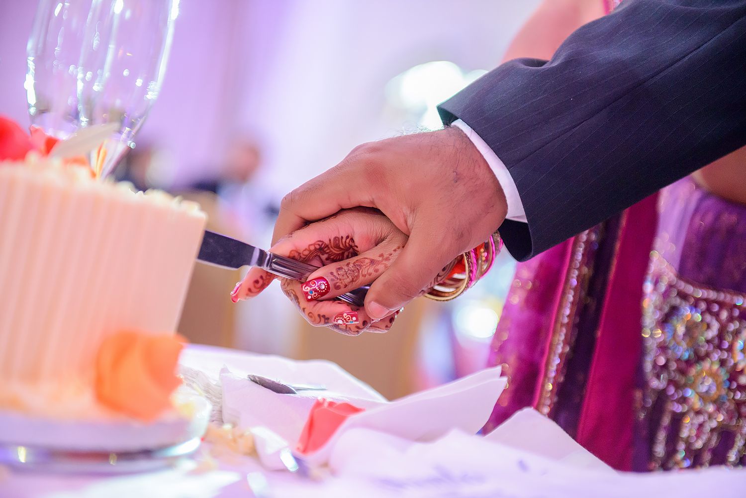 Hands cut into an ornate wedding cake with decorative pink details.