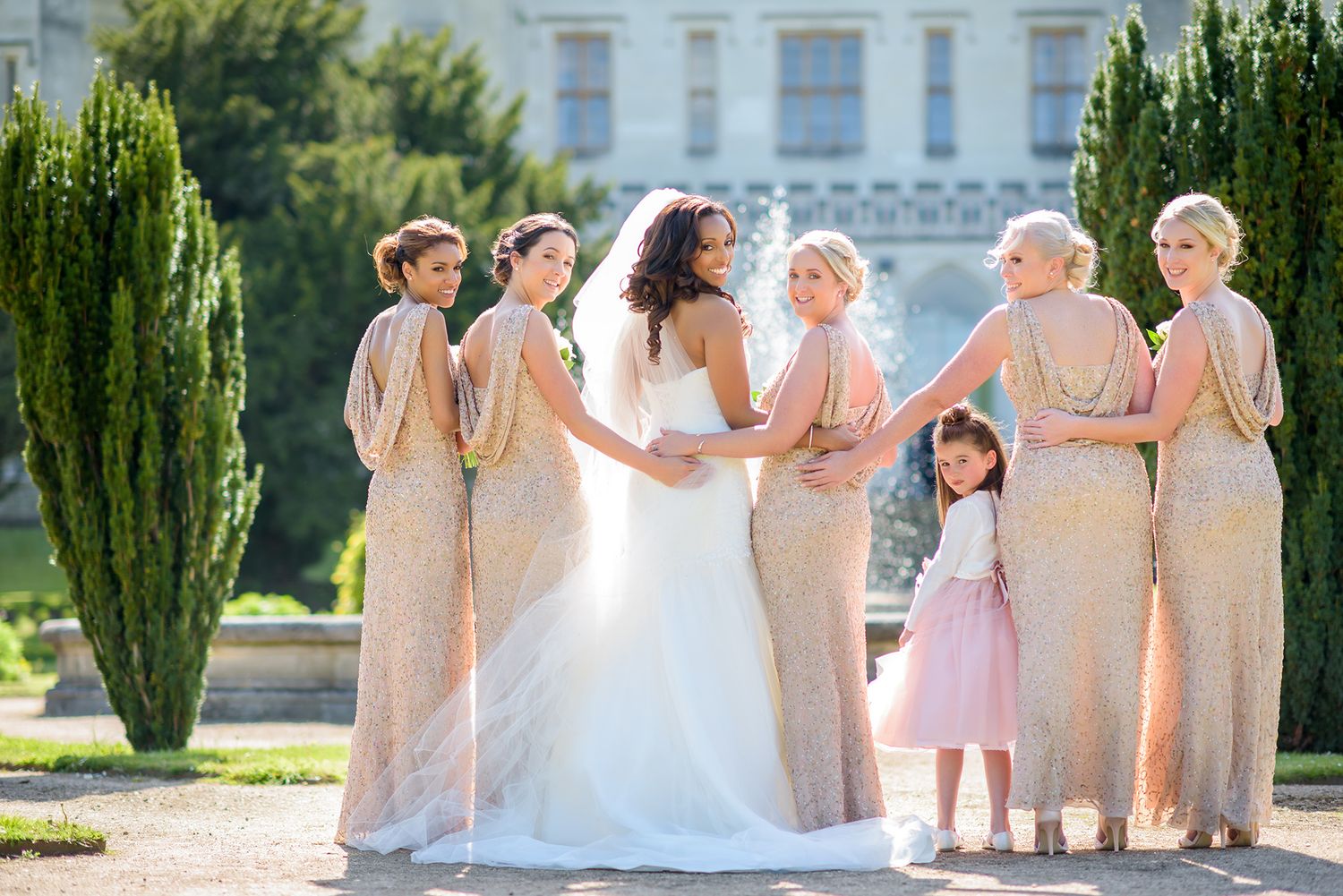 Bridesmaids in blush pink dresses standing together on mansion grounds.