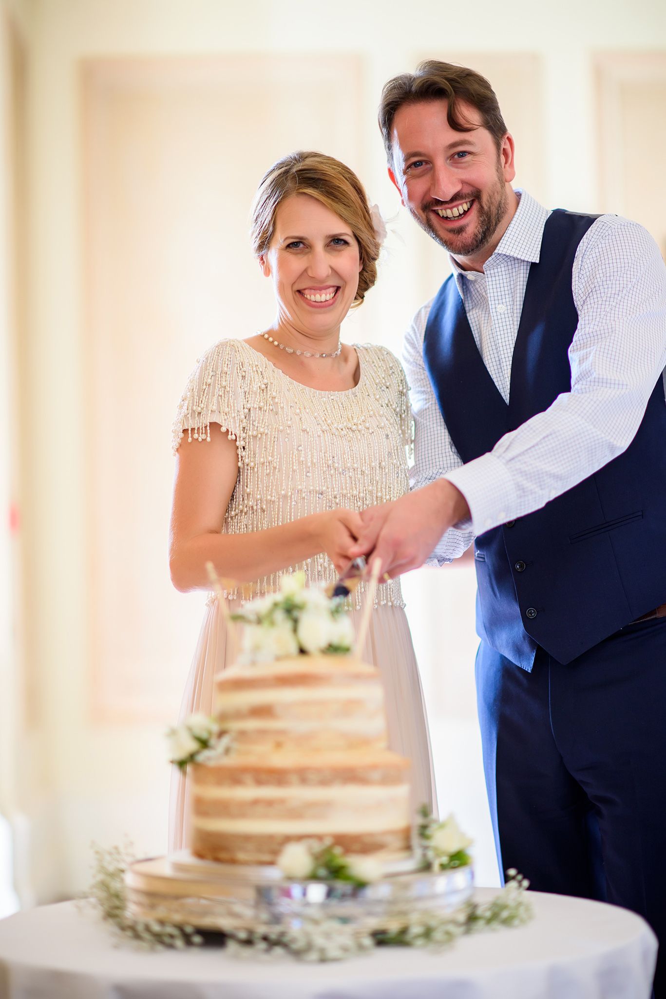 Couple cutting their rustic naked wedding cake decorated with fresh flowers.