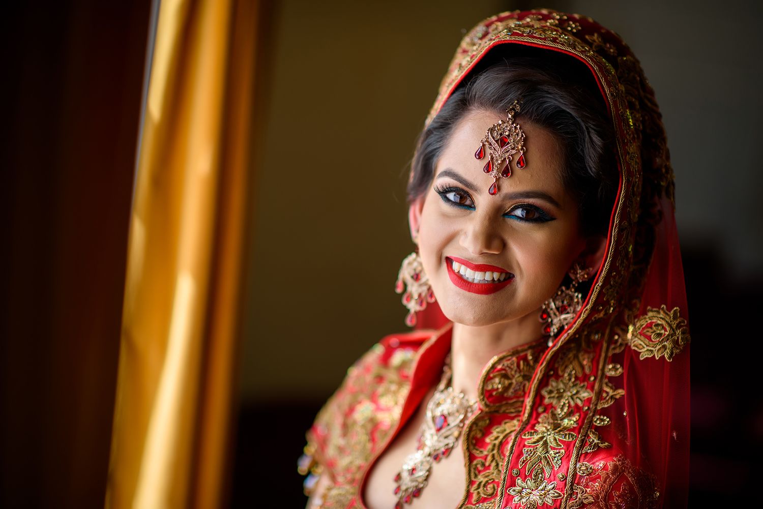 Beautiful traditional South Asian bridal attire with ornate jewelry and embroidered red dress.