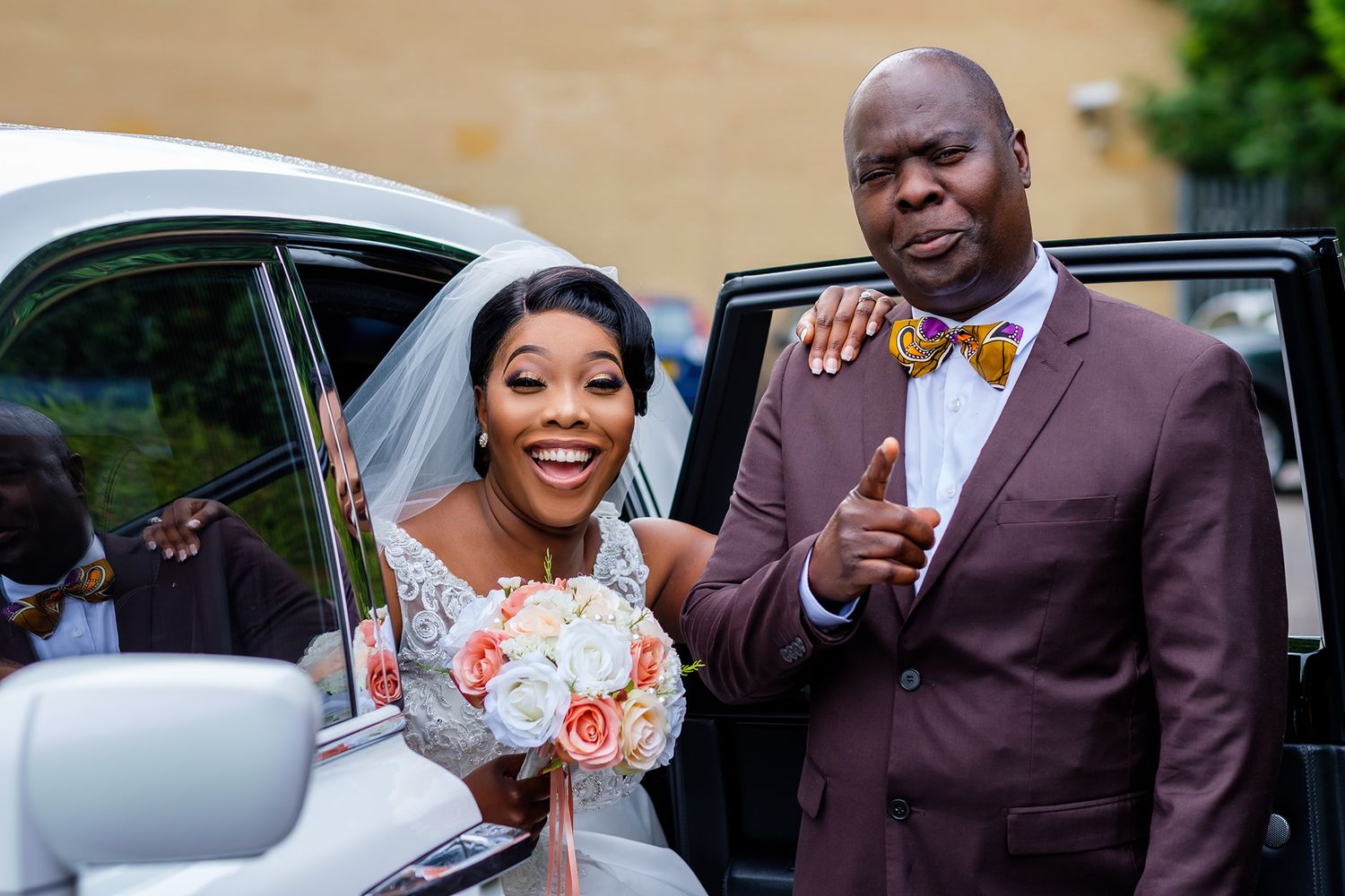 People in formal attire interacting beside luxury vehicles at a wedding.