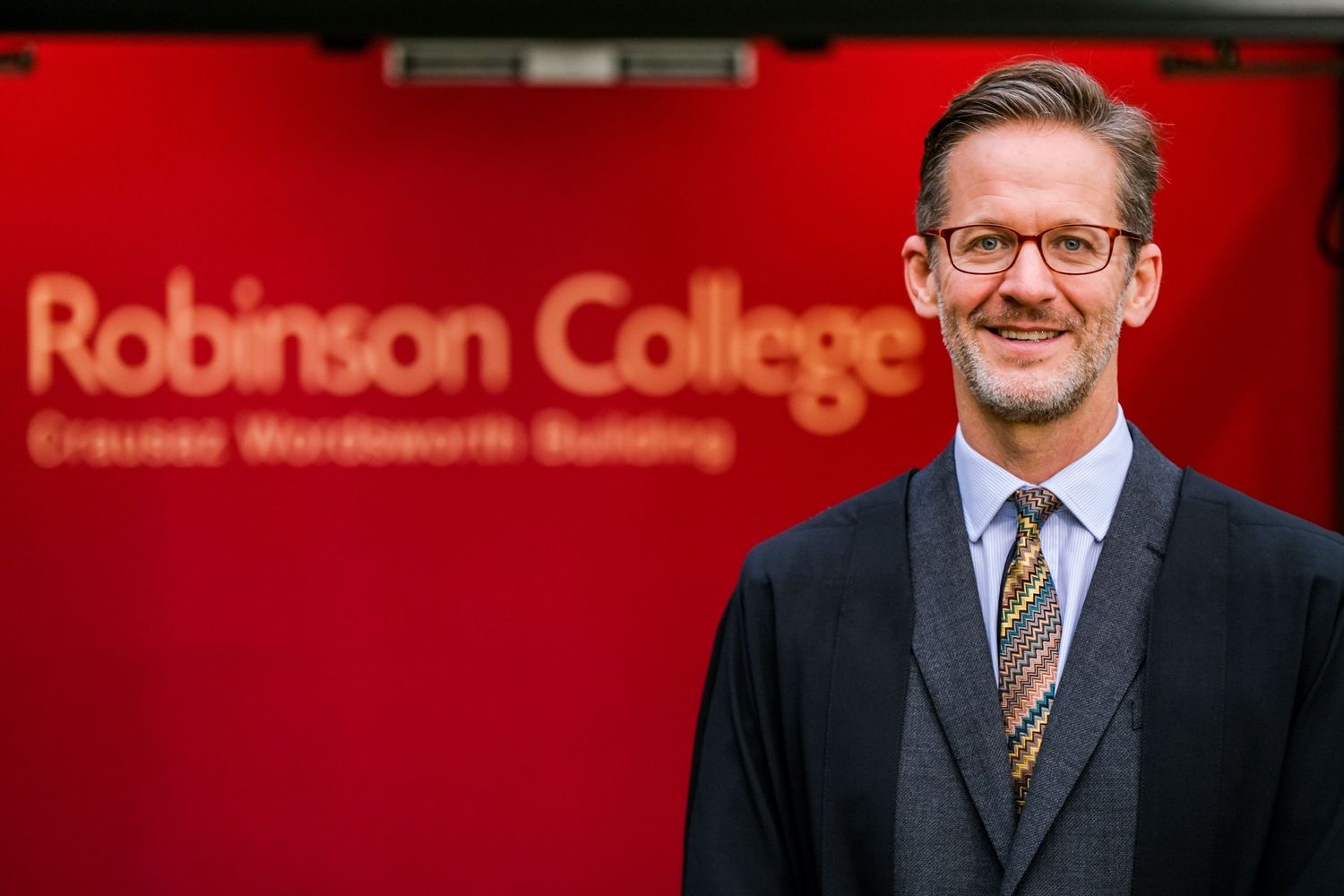Professional portrait of educators in business attire at Robinson College with signage visible in background.