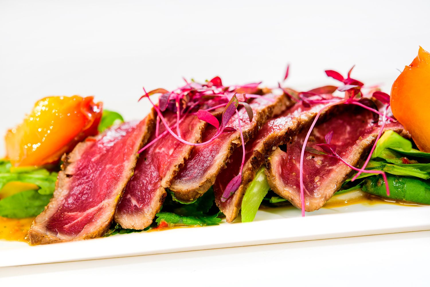 Seared tuna slices arranged on a white plate with colorful garnishes and microgreens.
