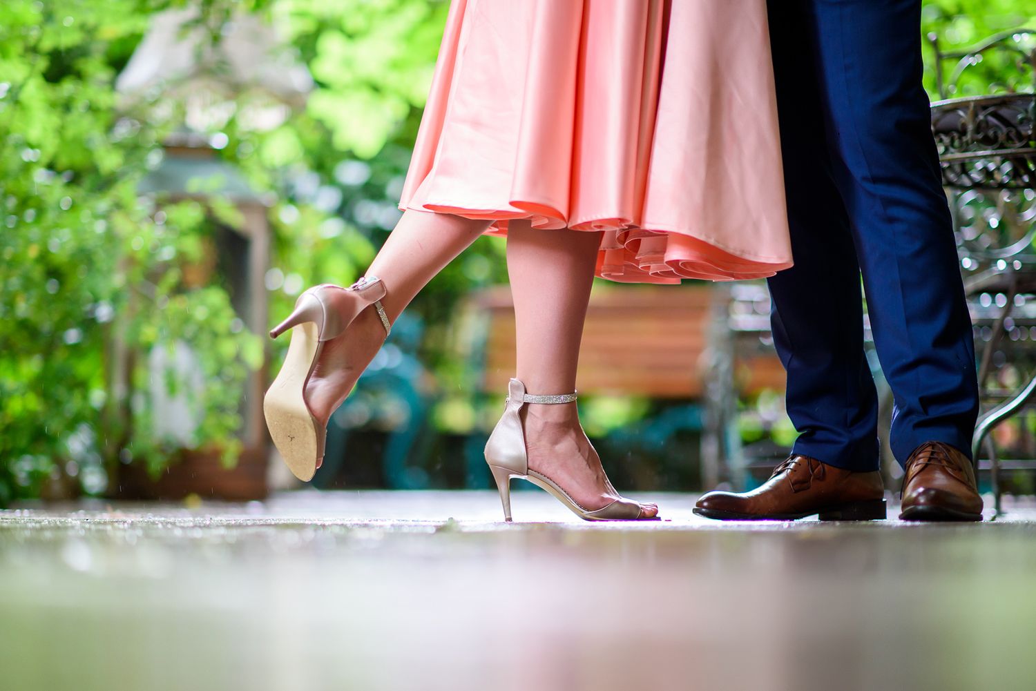 Close-up of formal footwear and dress hem against garden backdrop.