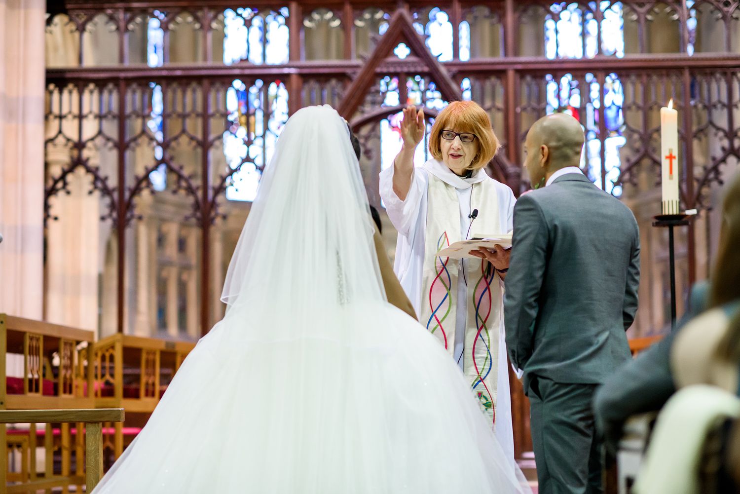 Wedding ceremony taking place in ornate church with stained glass windows.
