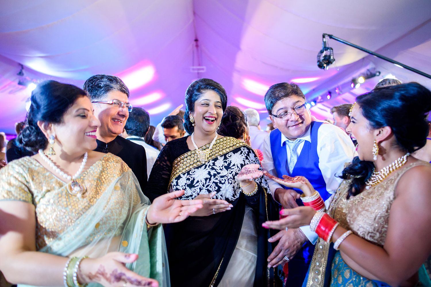Energetic crowd dancing and celebrating at a vibrant wedding reception with colorful purple lighting effects.