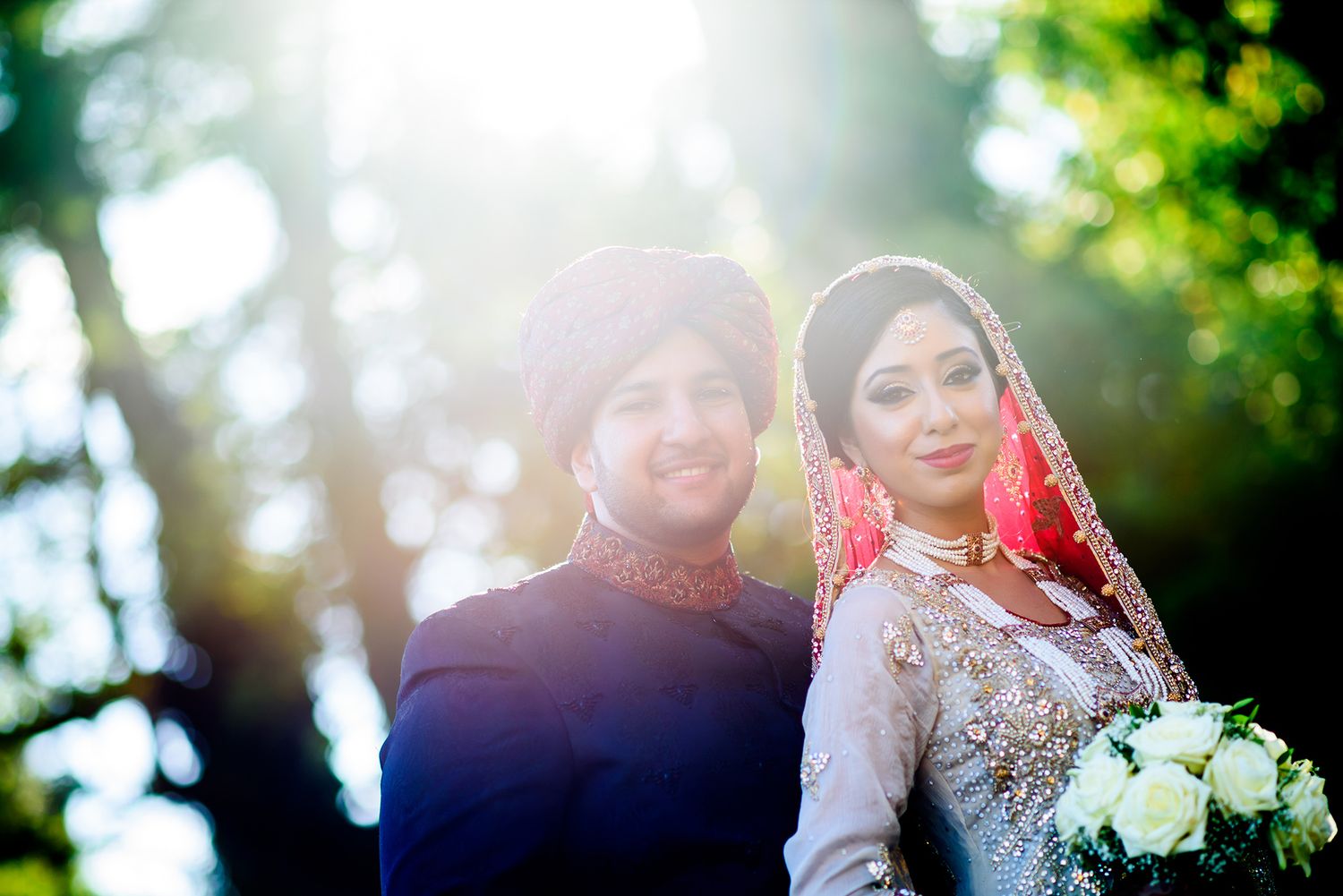 Sunlit outdoor wedding portrait with couple in traditional South Asian dress.