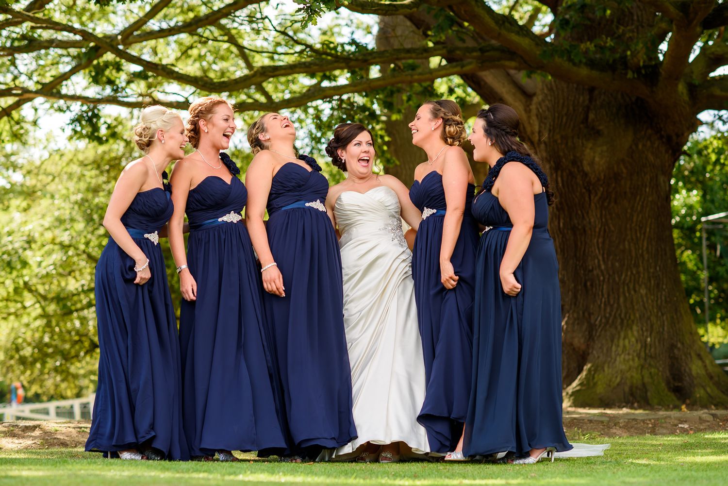 Wedding party poses under majestic oak tree wearing navy blue and white attire.