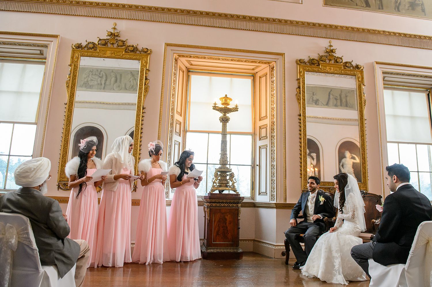 Elegant wedding celebration in a luxurious ballroom with gold-framed mirrors and pink accents.