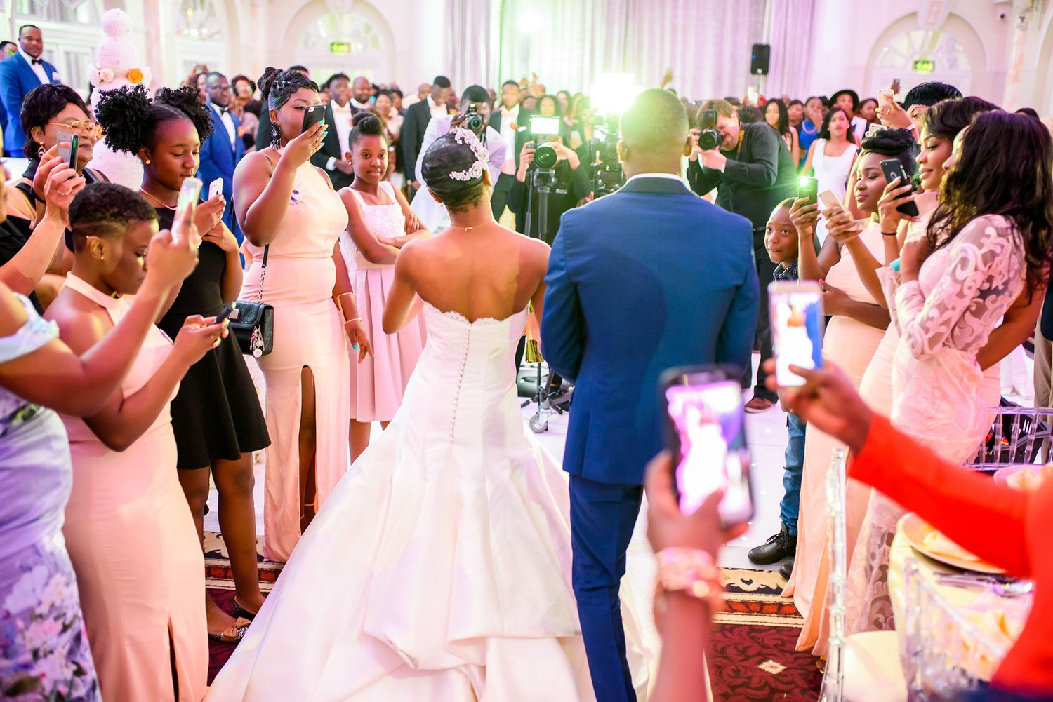 Wedding reception dance floor filled with guests celebrating under pink lighting.