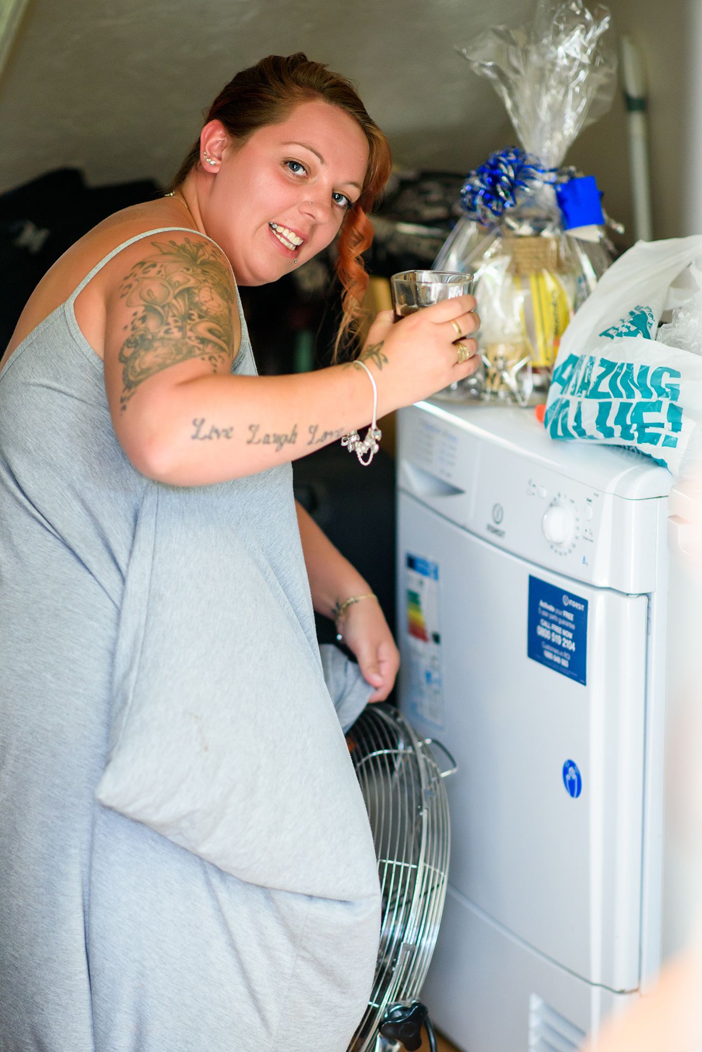 Person in gray shirt poses playfully next to a white refrigerator.