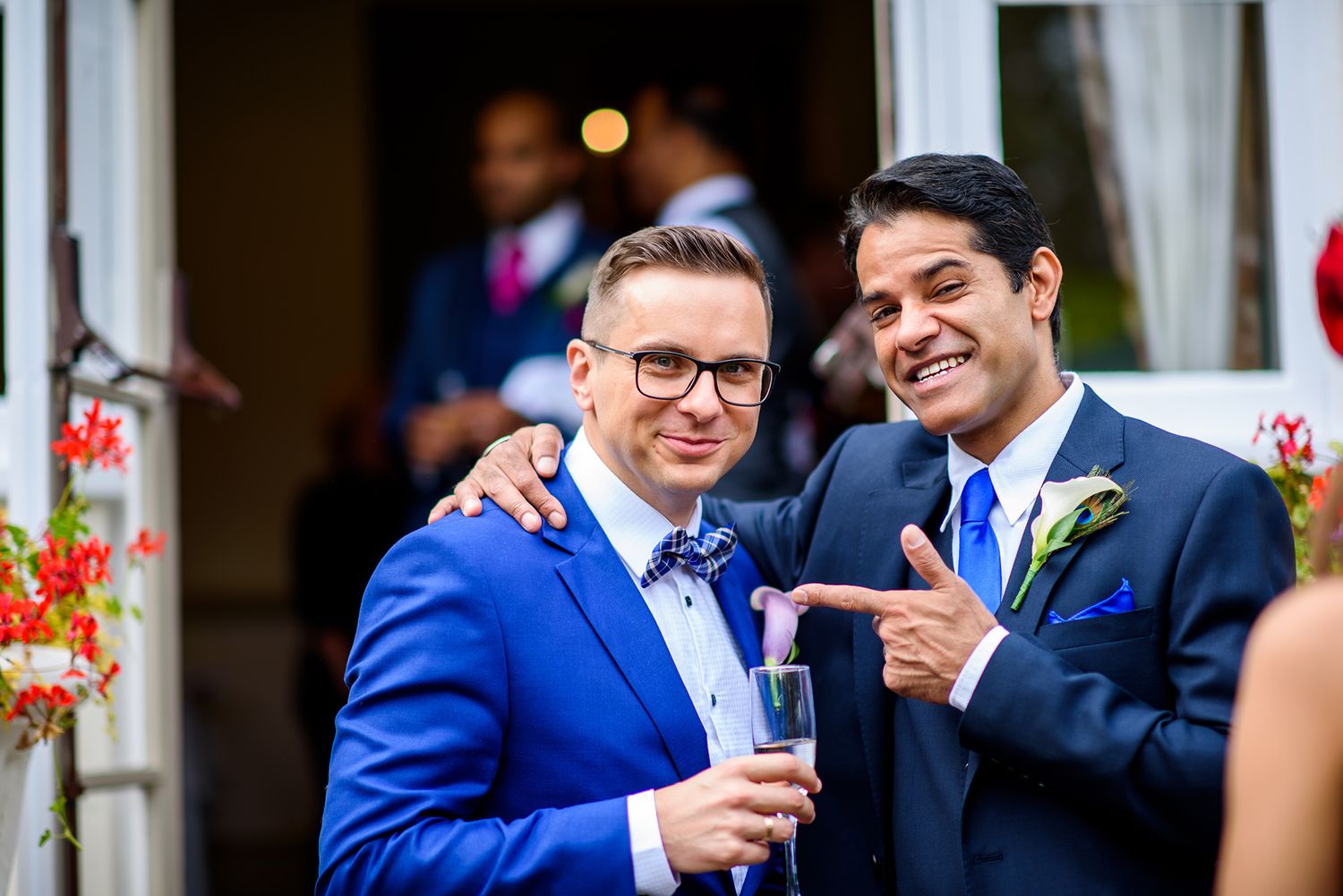 Two wedding guests in suits share a lighthearted moment with drinks at the reception.