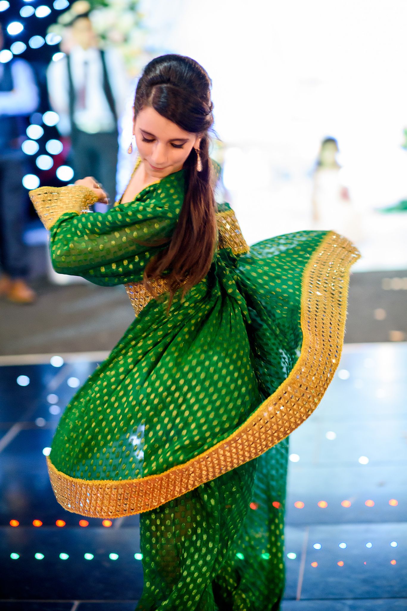 Two dancers perform in traditional outfits with a bright green and gold dress swirling during a cultural dance performance.
