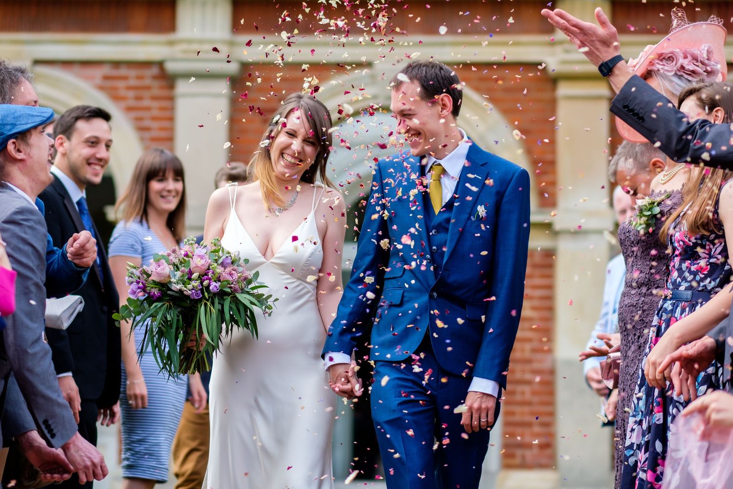 Guests throw blue and pink confetti during an outdoor wedding celebration.