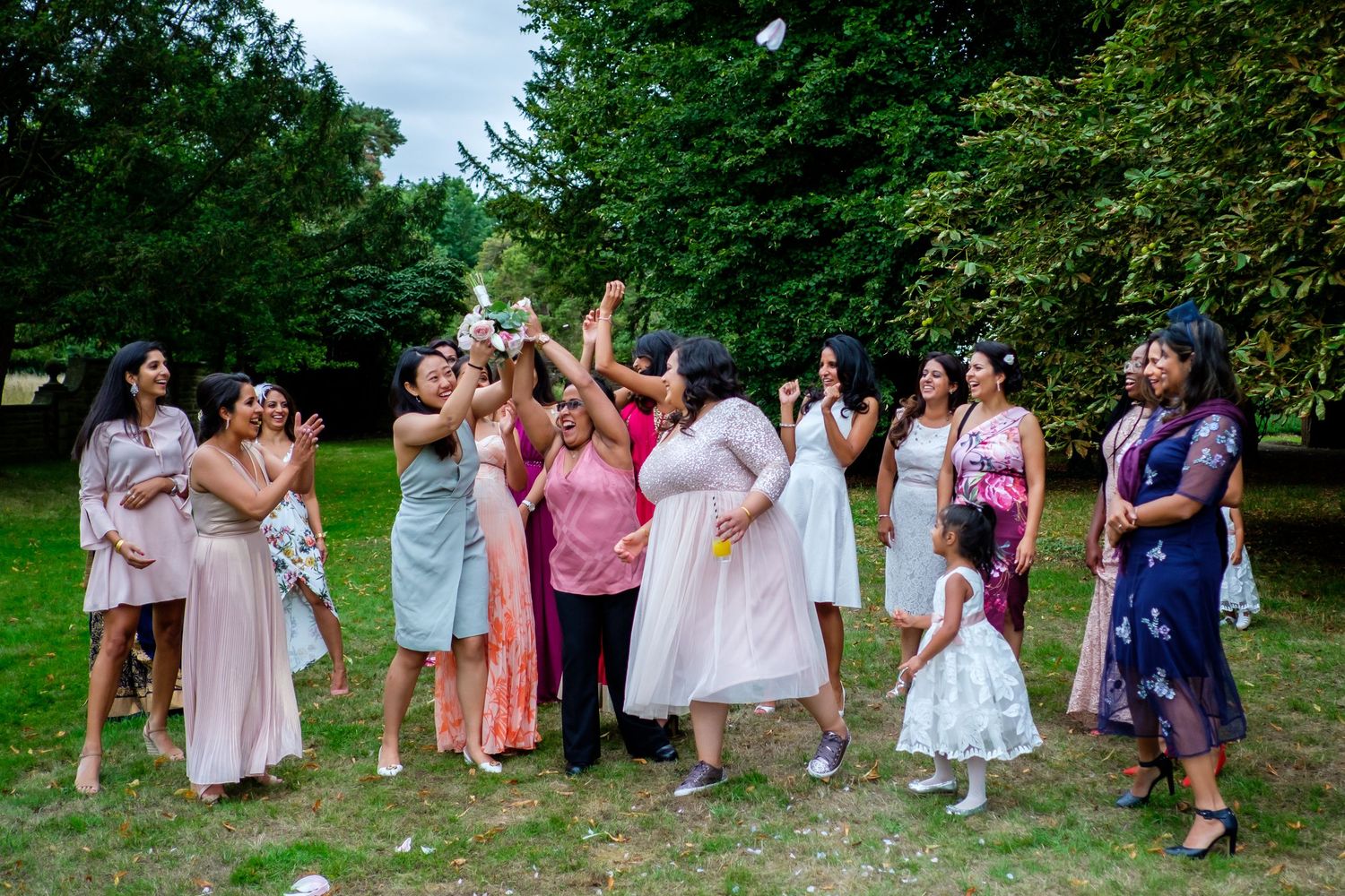 Wedding party poses for group photos on green hillside during summer celebration.