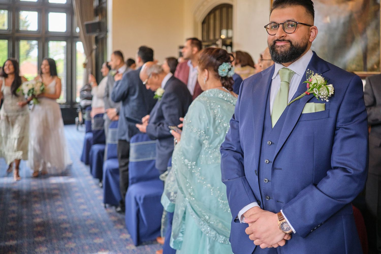 Wedding guests stand in a formal venue wearing formal attire.