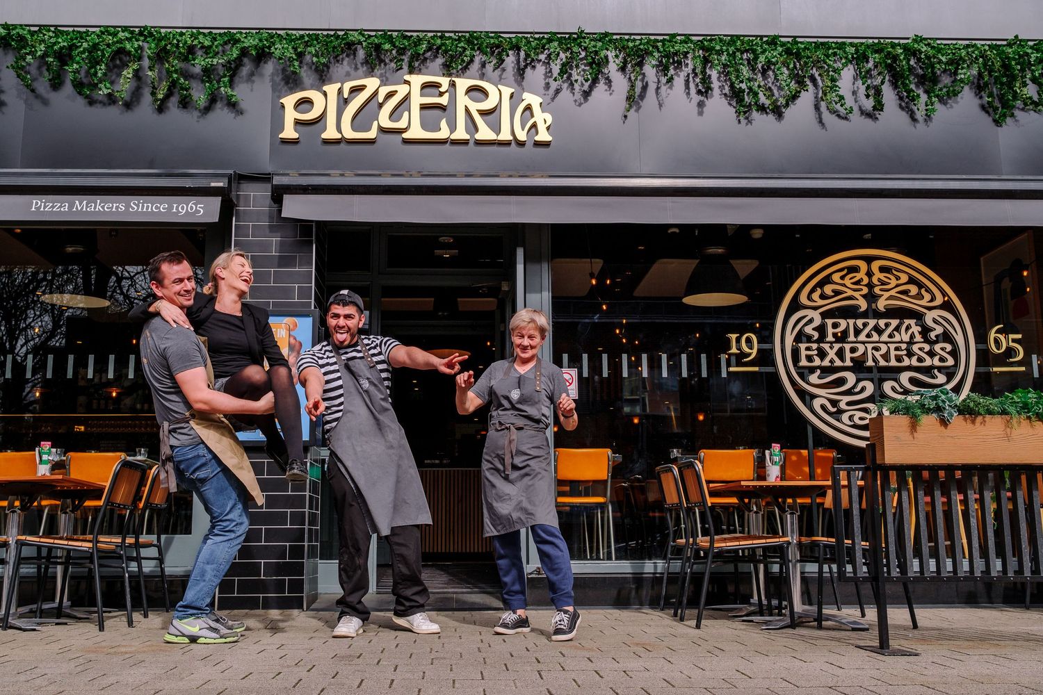Pizza Express storefront with outdoor seating area and decorative greenery.