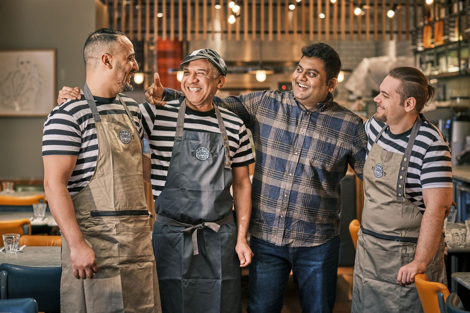 Staff members in aprons and casual attire standing together in a restaurant kitchen.