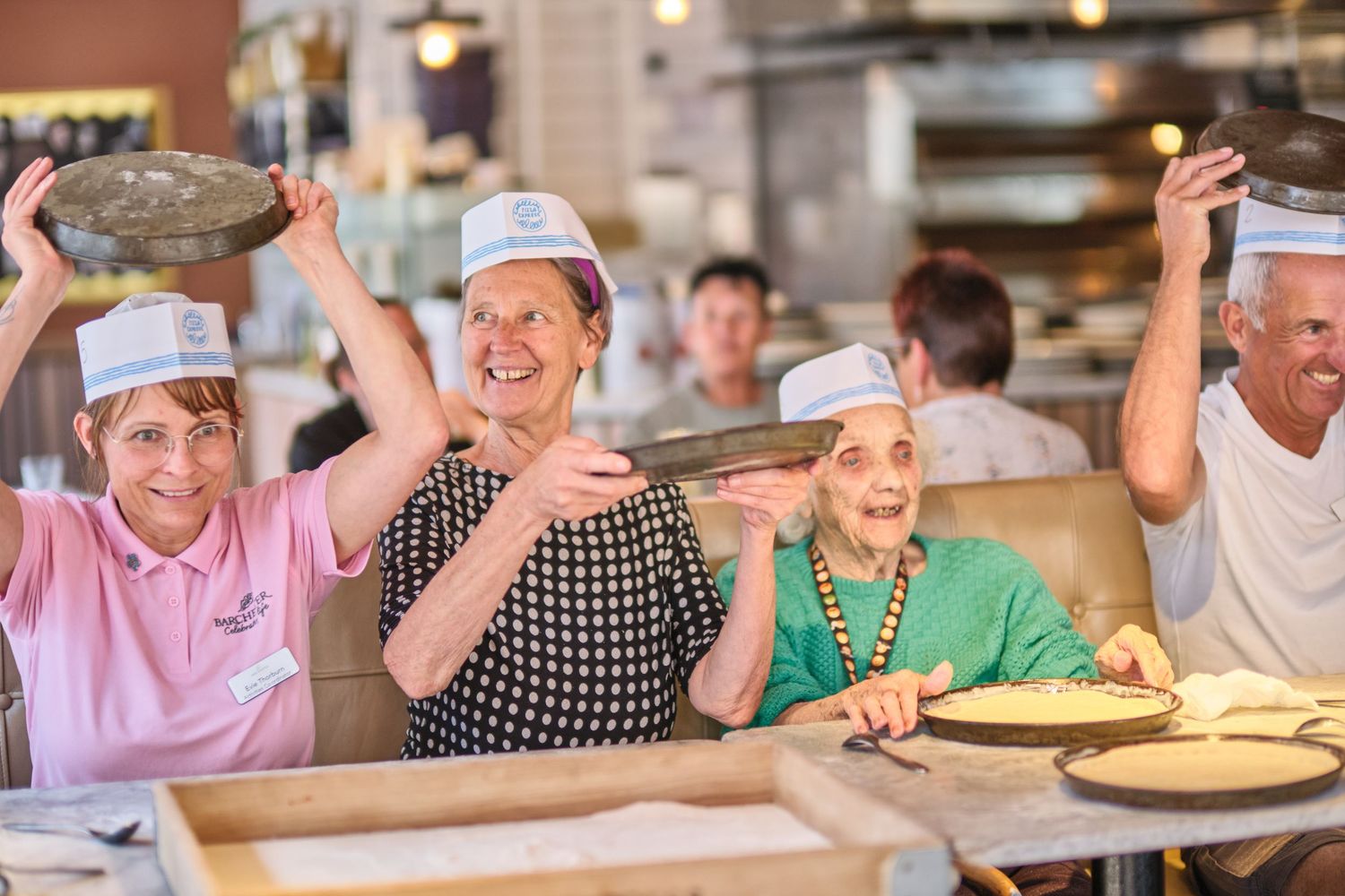 Restaurant patrons seated at a long table participating in what appears to be a pizza-making event.