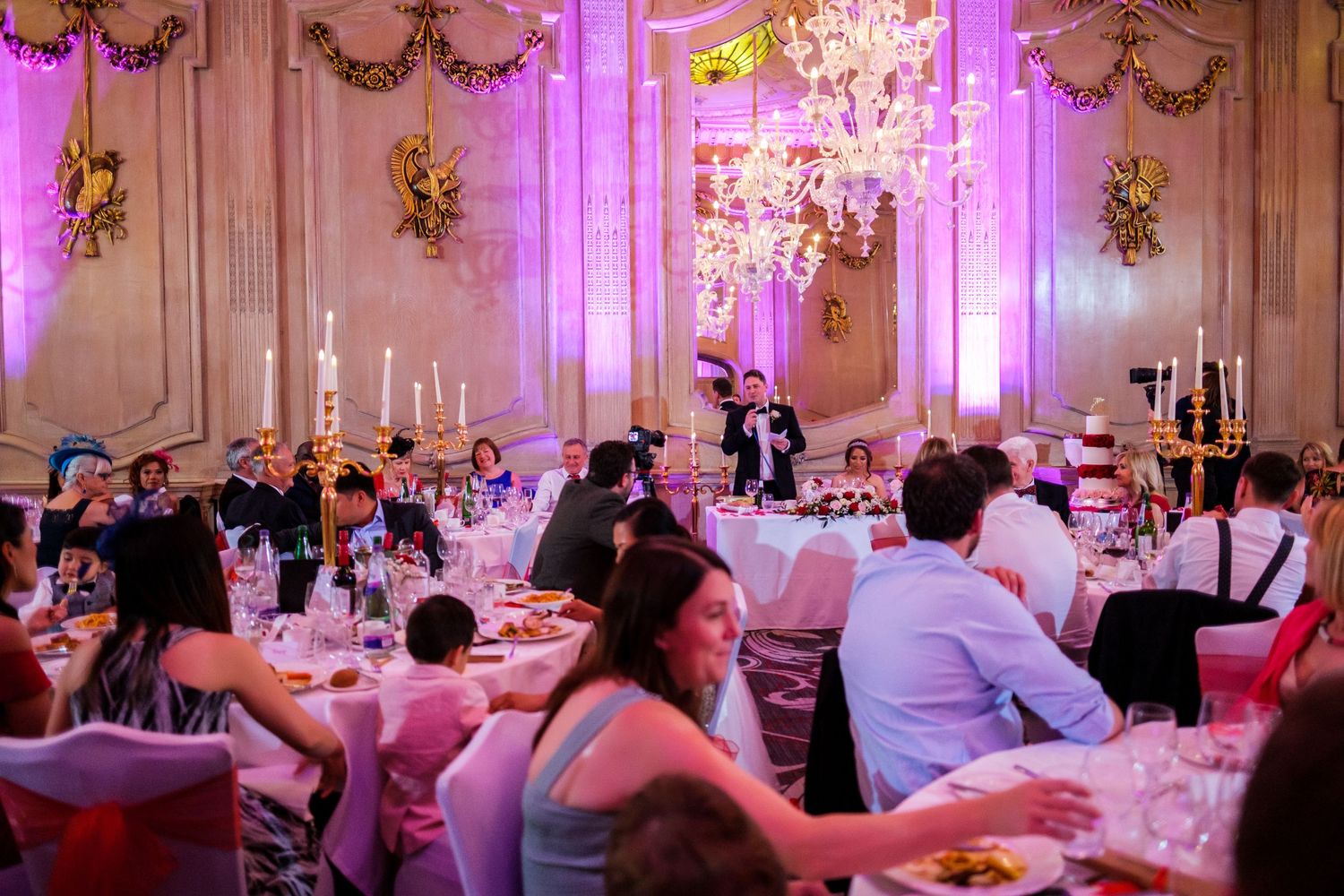 Elegant ballroom reception with pink uplighting, crystal chandeliers and decorated tables.