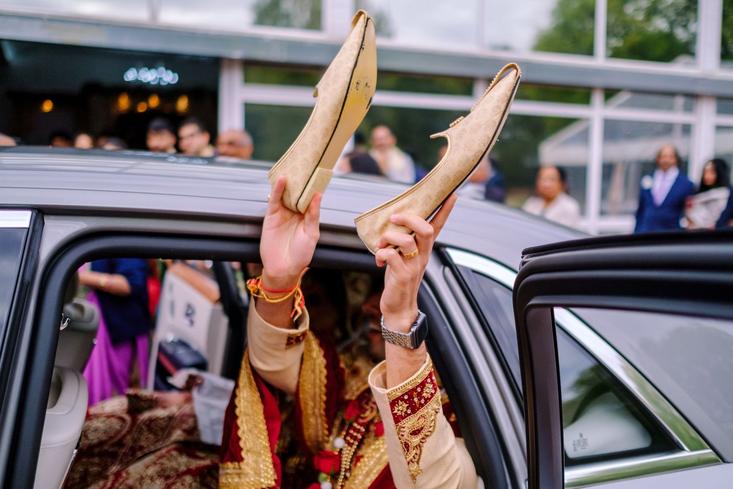 Celebratory moment showing raised hands through car window during Indian wedding festivities.
