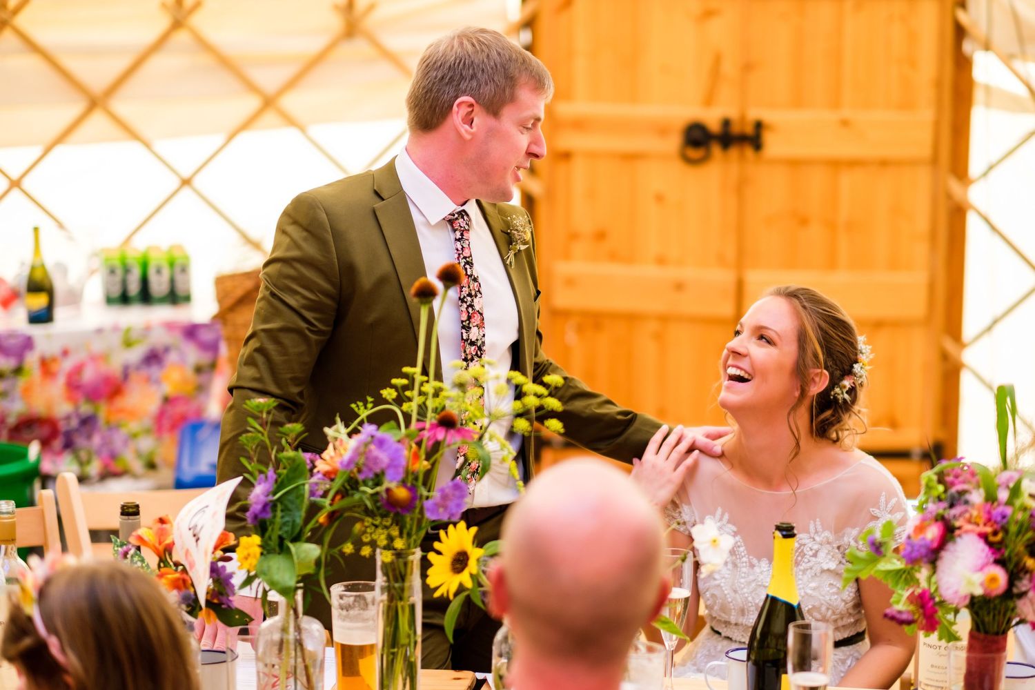 Wedding guests enjoy a lively reception in a rustic barn venue decorated with colorful floral arrangements.
