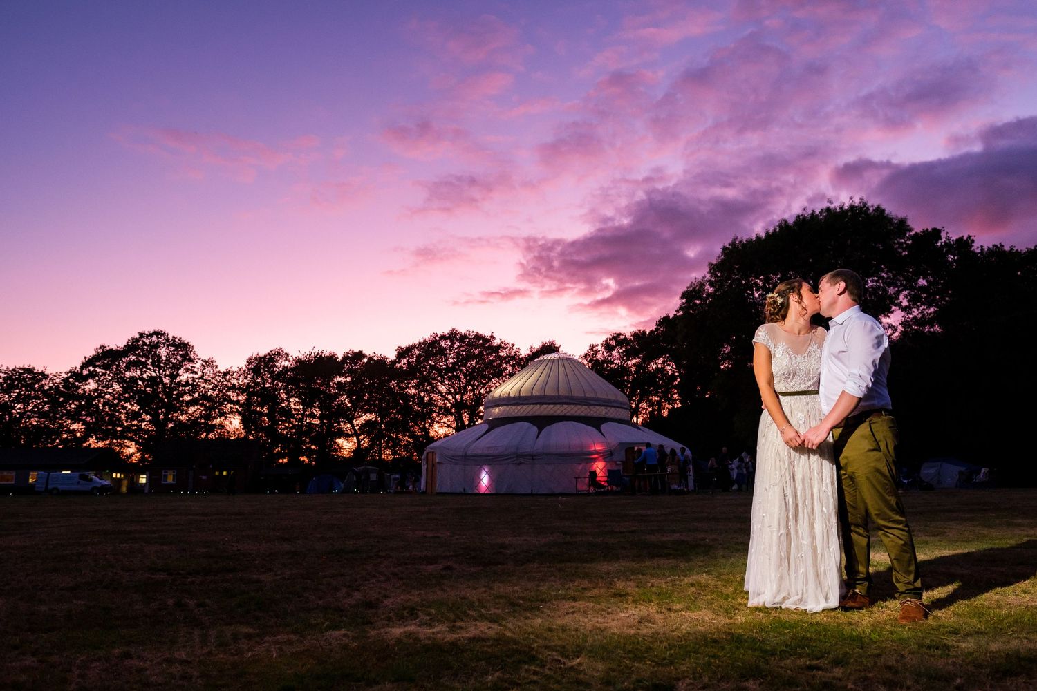 Panoramic sunset view with silhouettes of trees and wedding decorations against a purple and pink sky.