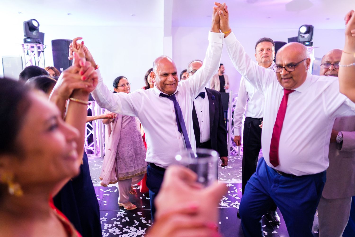 Celebration on the dance floor with guests raising hands amid confetti and party lights.