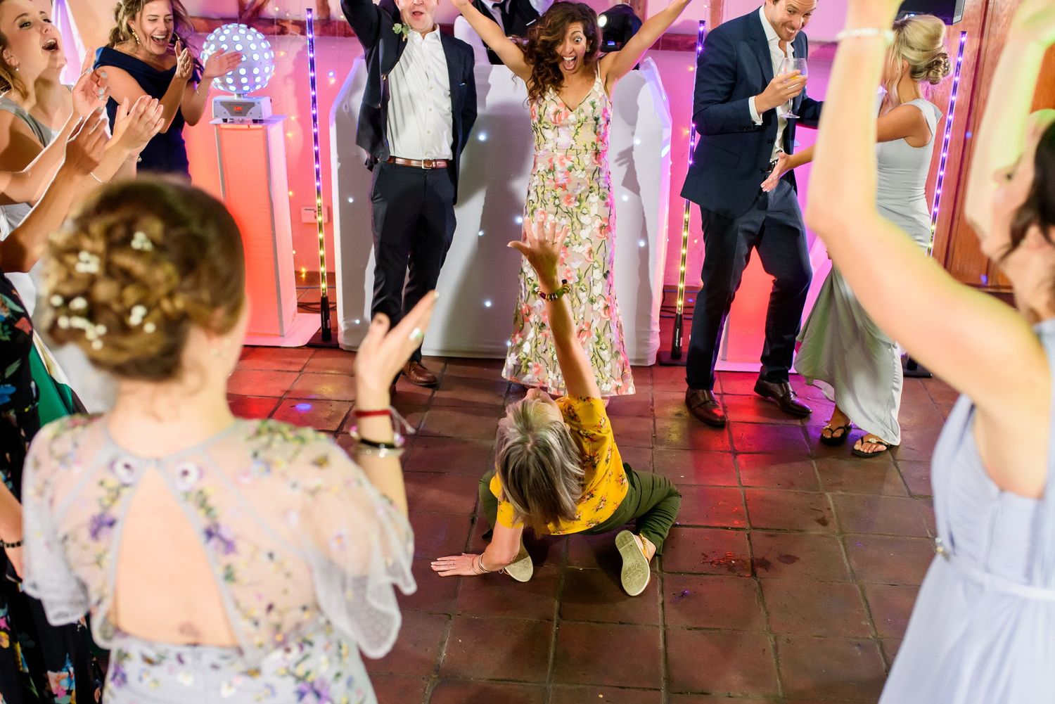 Wedding reception dance floor filled with guests celebrating under pink lighting.