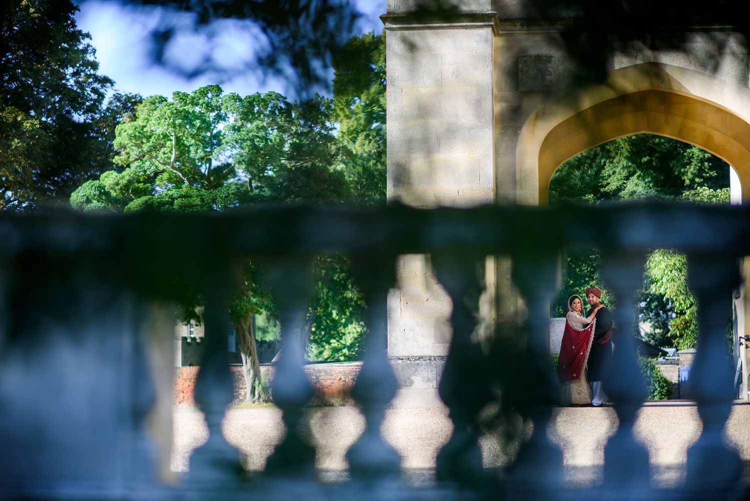 Artistic wedding portrait through decorative balustrade with arched architecture.