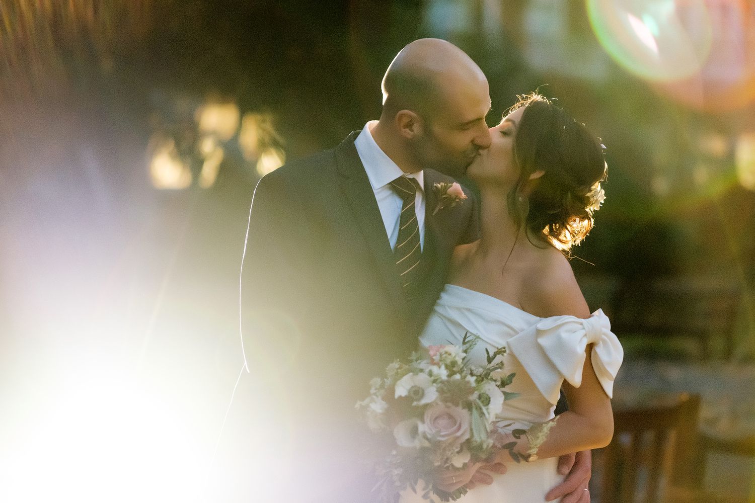 Romantic sunset wedding photo showing a couple embracing with warm golden light in the background.
