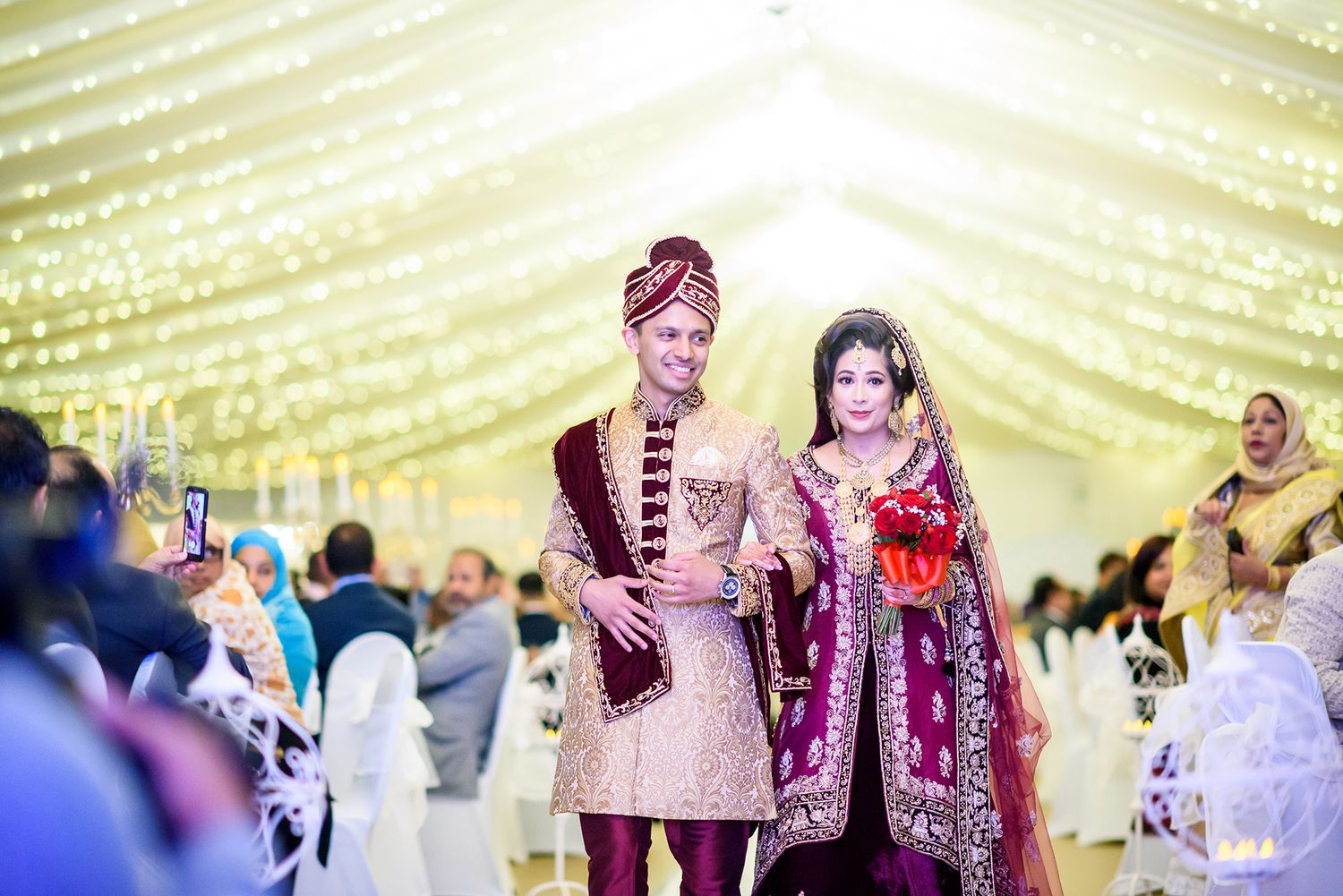 Wedding celebration under a beautifully lit tent with traditional South Asian attire.