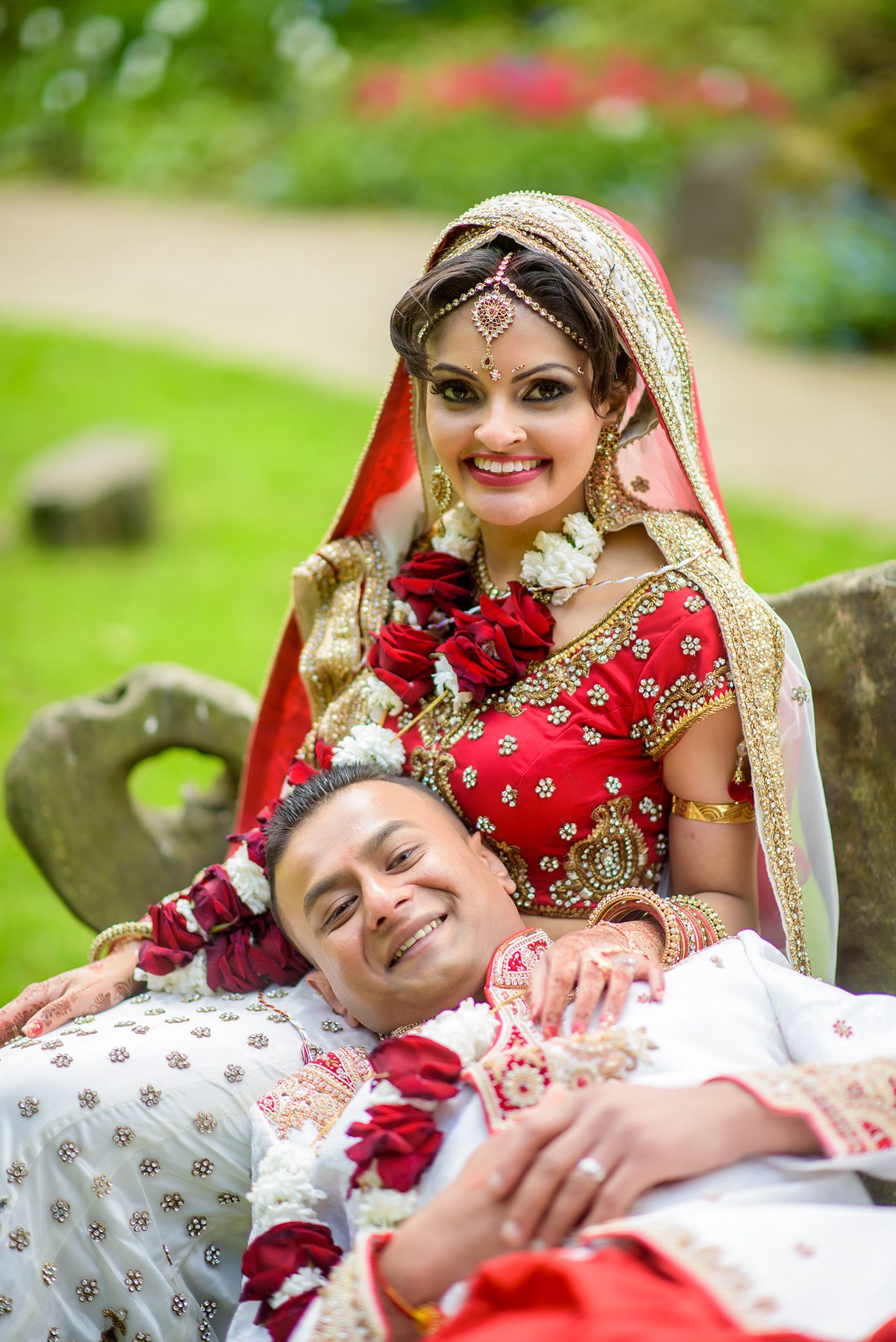 Couple in traditional Indian wedding attire relaxing on grass during outdoor photoshoot.