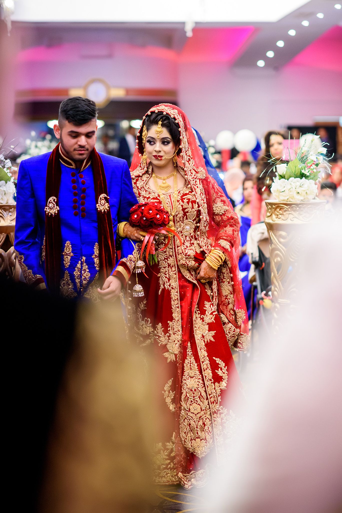 Traditional Indian wedding procession with bride in red and gold lehenga and guests in blue attire.