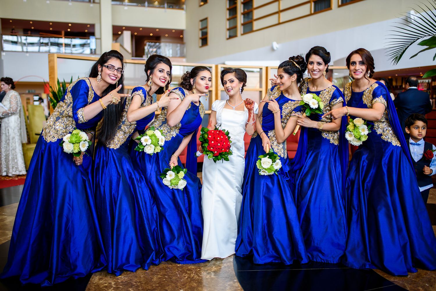 Wedding party in royal blue dresses and white gown lined up in grand venue.
