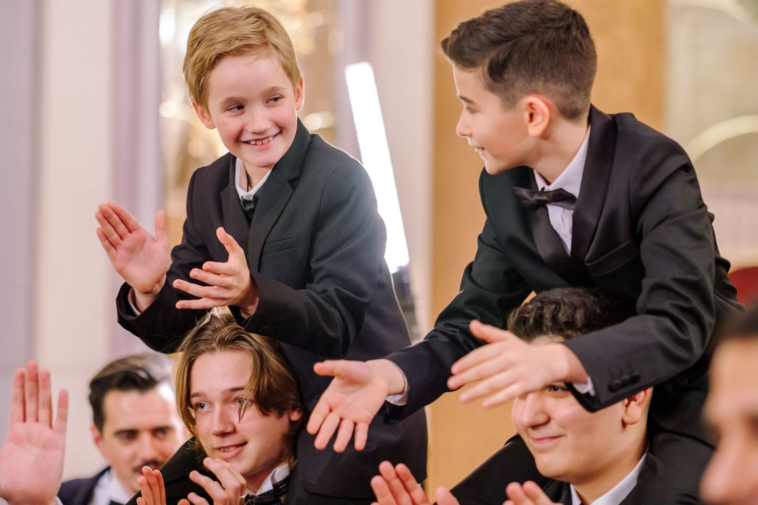 Group of formally dressed people in black suits and ties laughing and gesturing at a social gathering.
