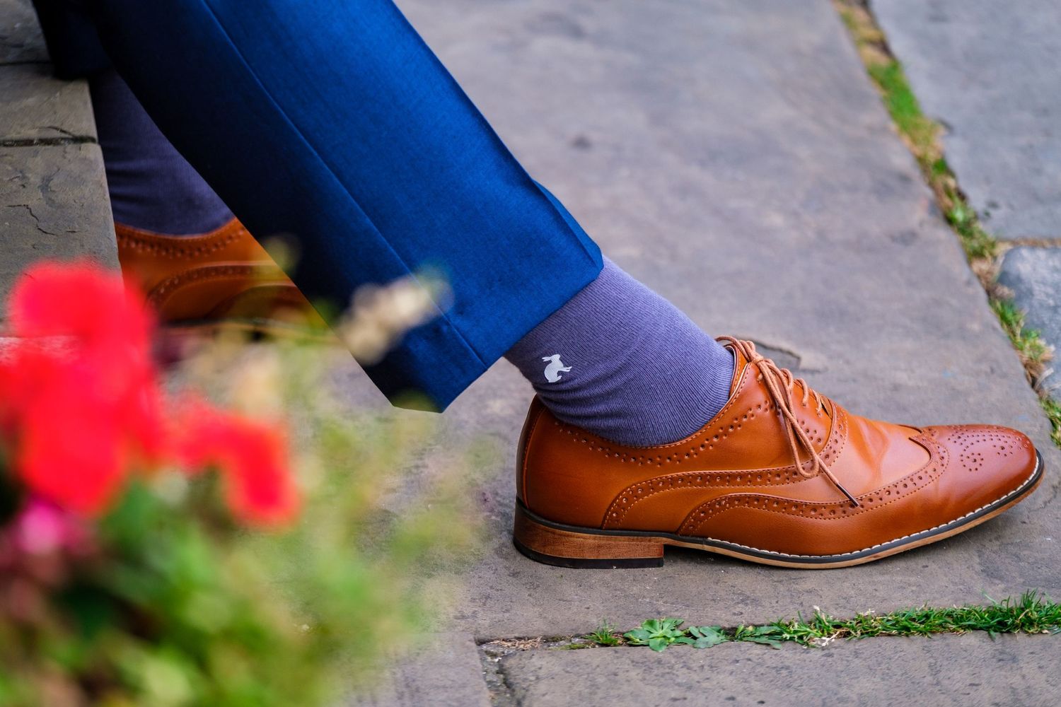 Detail shot of brown leather dress shoes and blue suit pants on stone pavement.