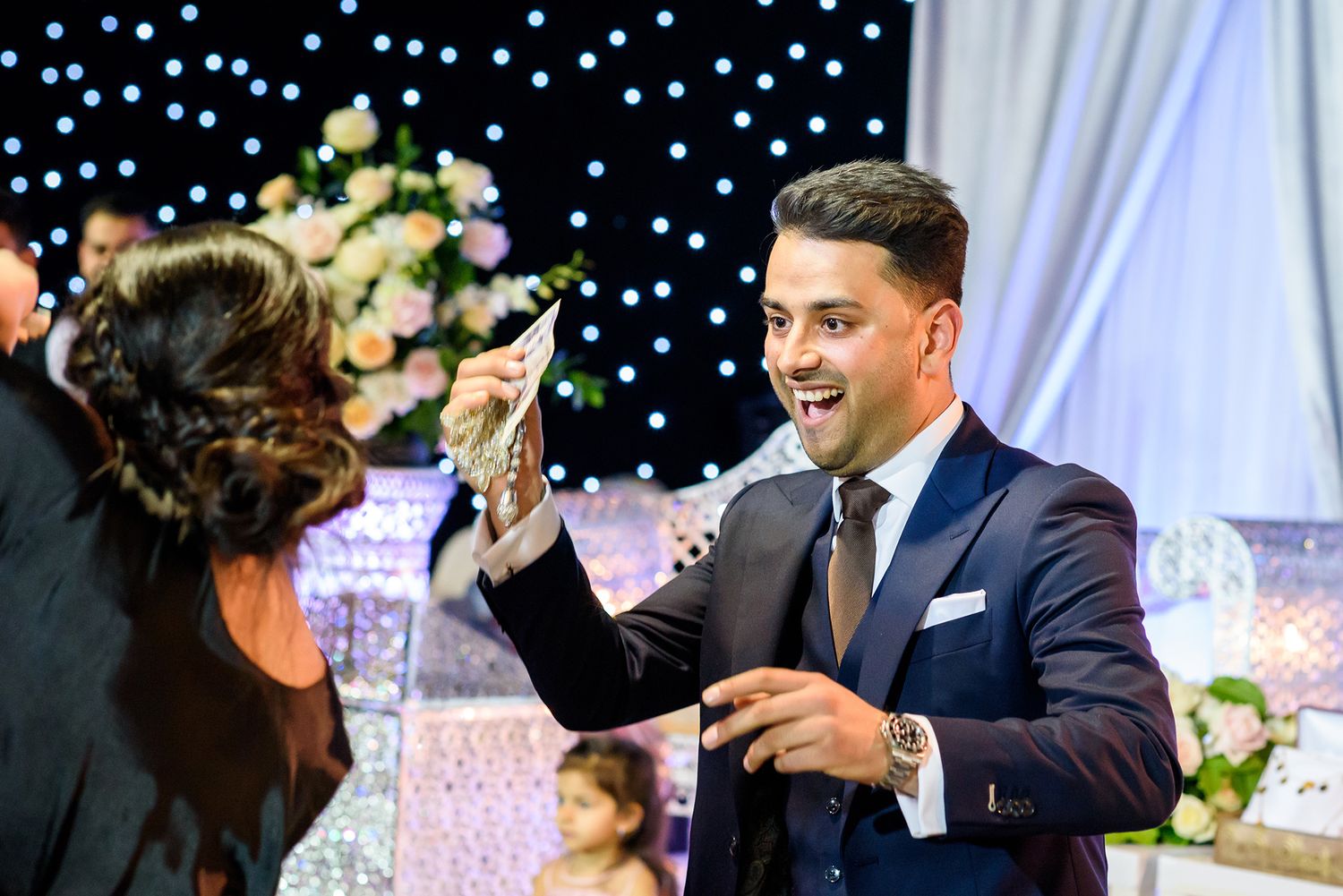 Elegant indoor wedding celebration with decorative white draping and twinkling lights in the background.