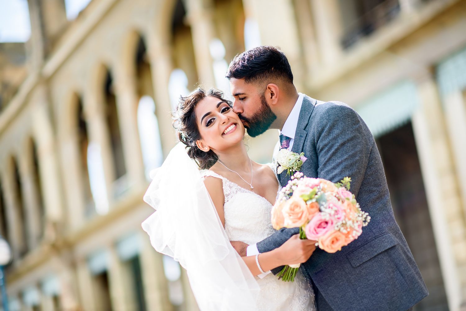 Wedding couple embracing in front of a classical stone building with elegant architecture.