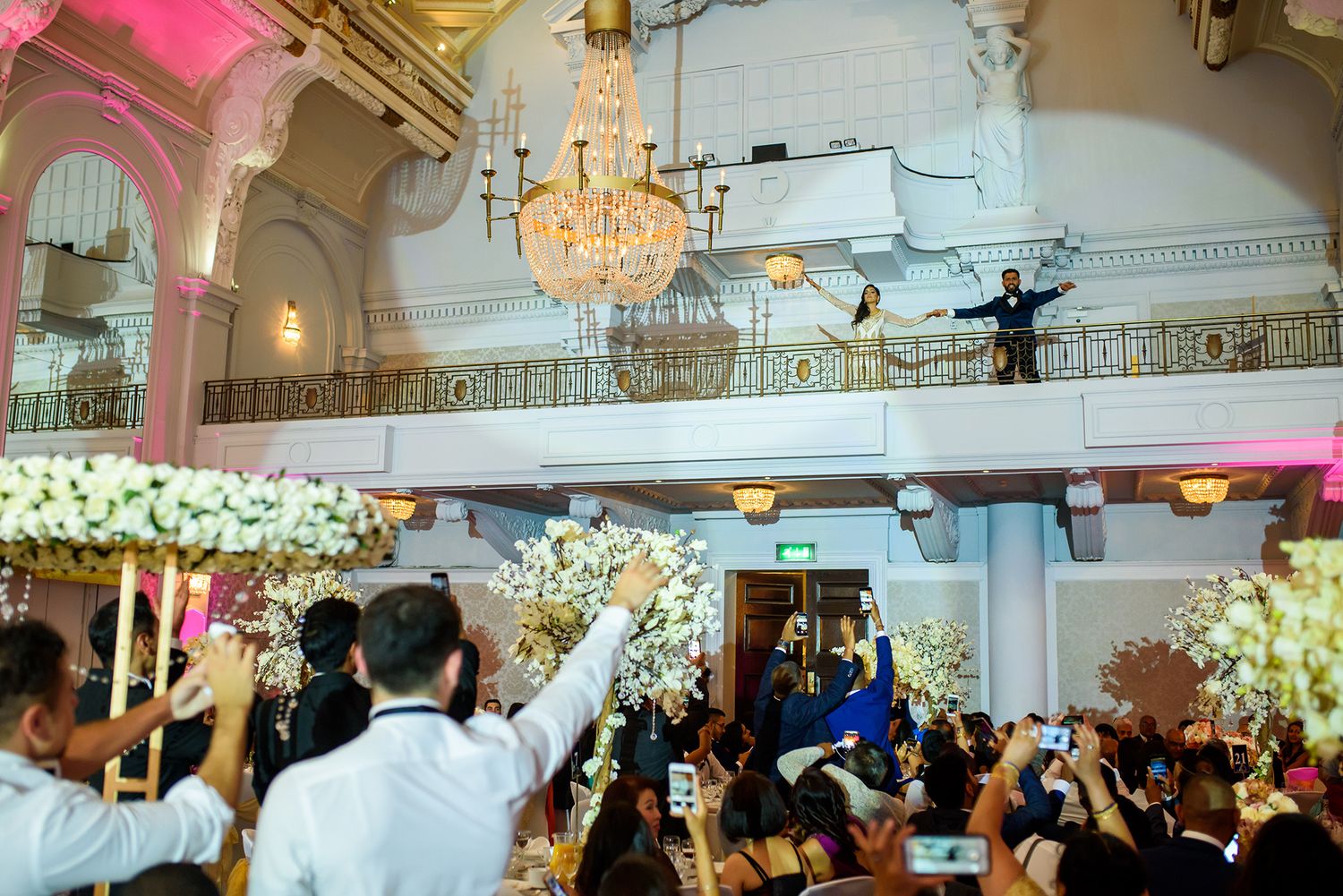 Large wedding reception hall decorated with chandeliers and floral arrangements.