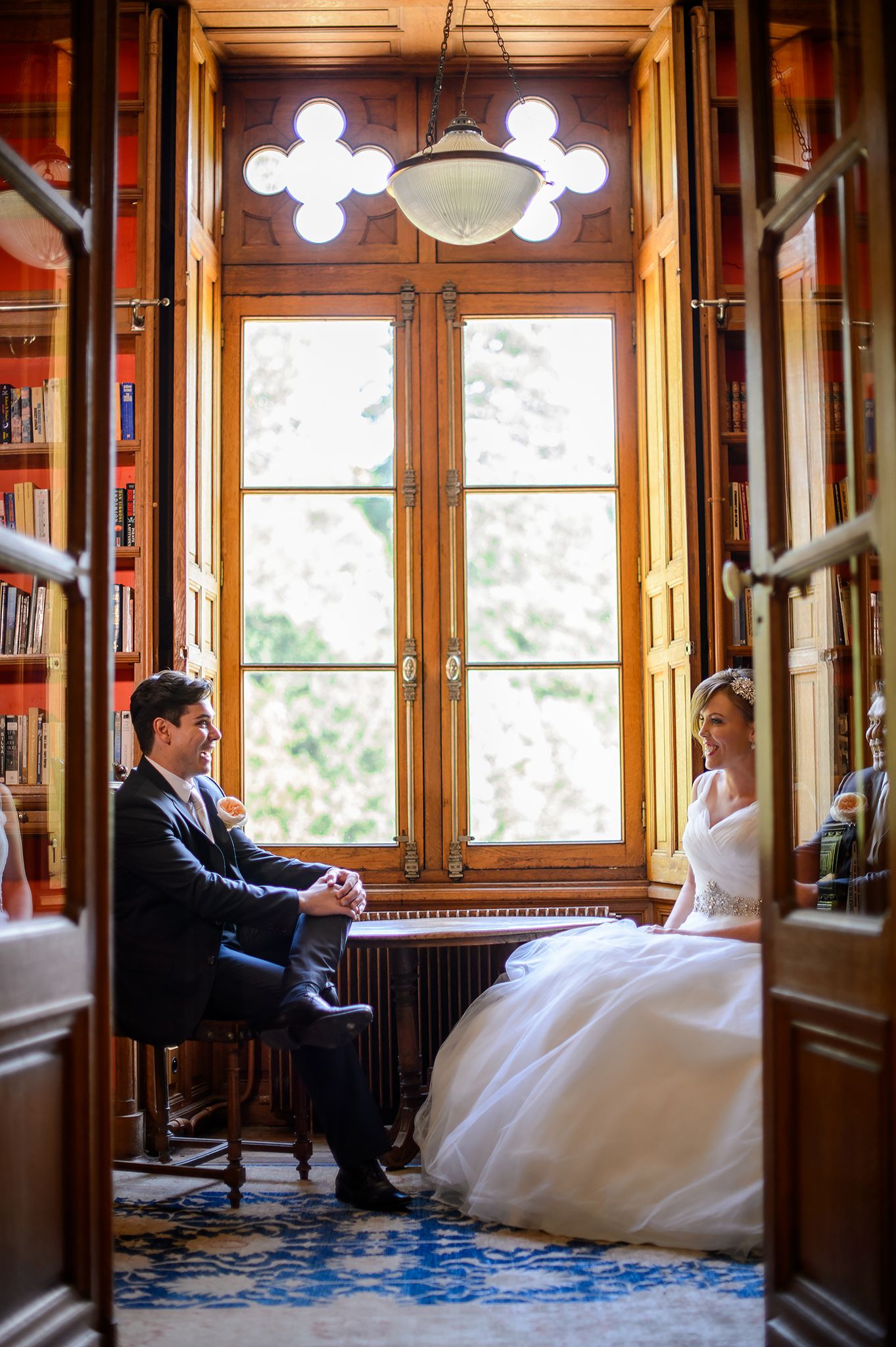 Elegant library setting with wood paneling and stained glass windows frames wedding couple.