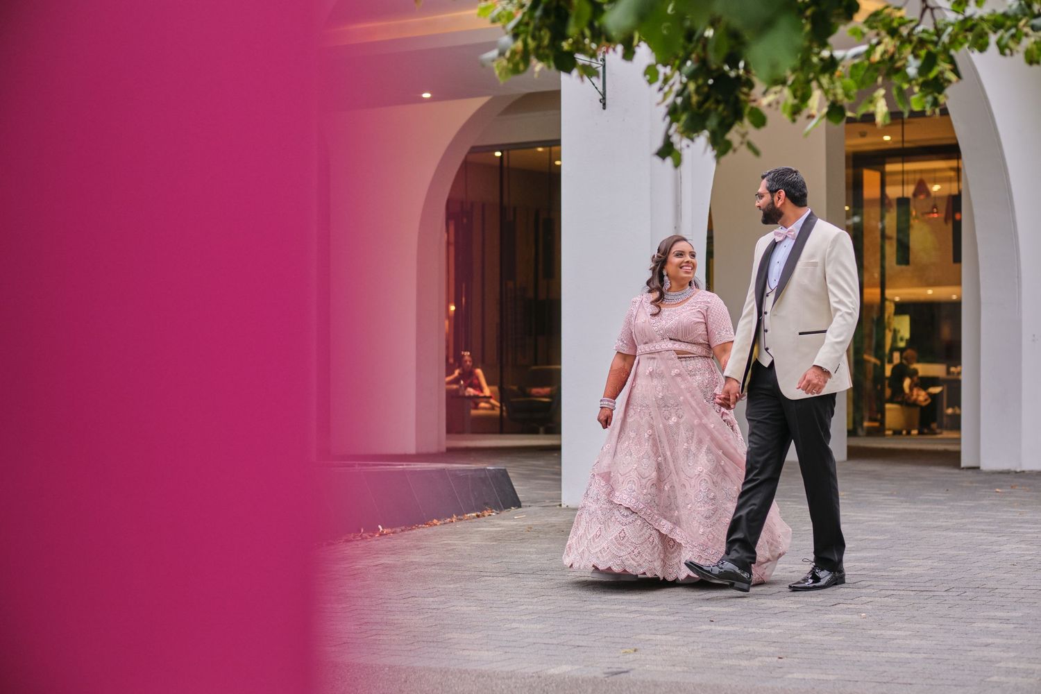 Couple walking through pink-tinted archways during wedding photoshoot.