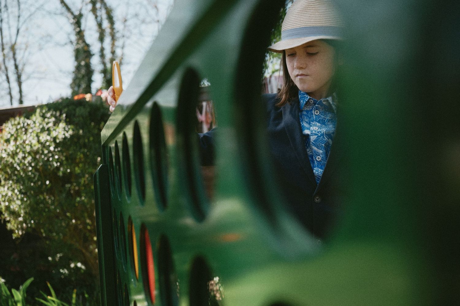 Outdoor wedding scene framed through green foliage with a white hat visible.