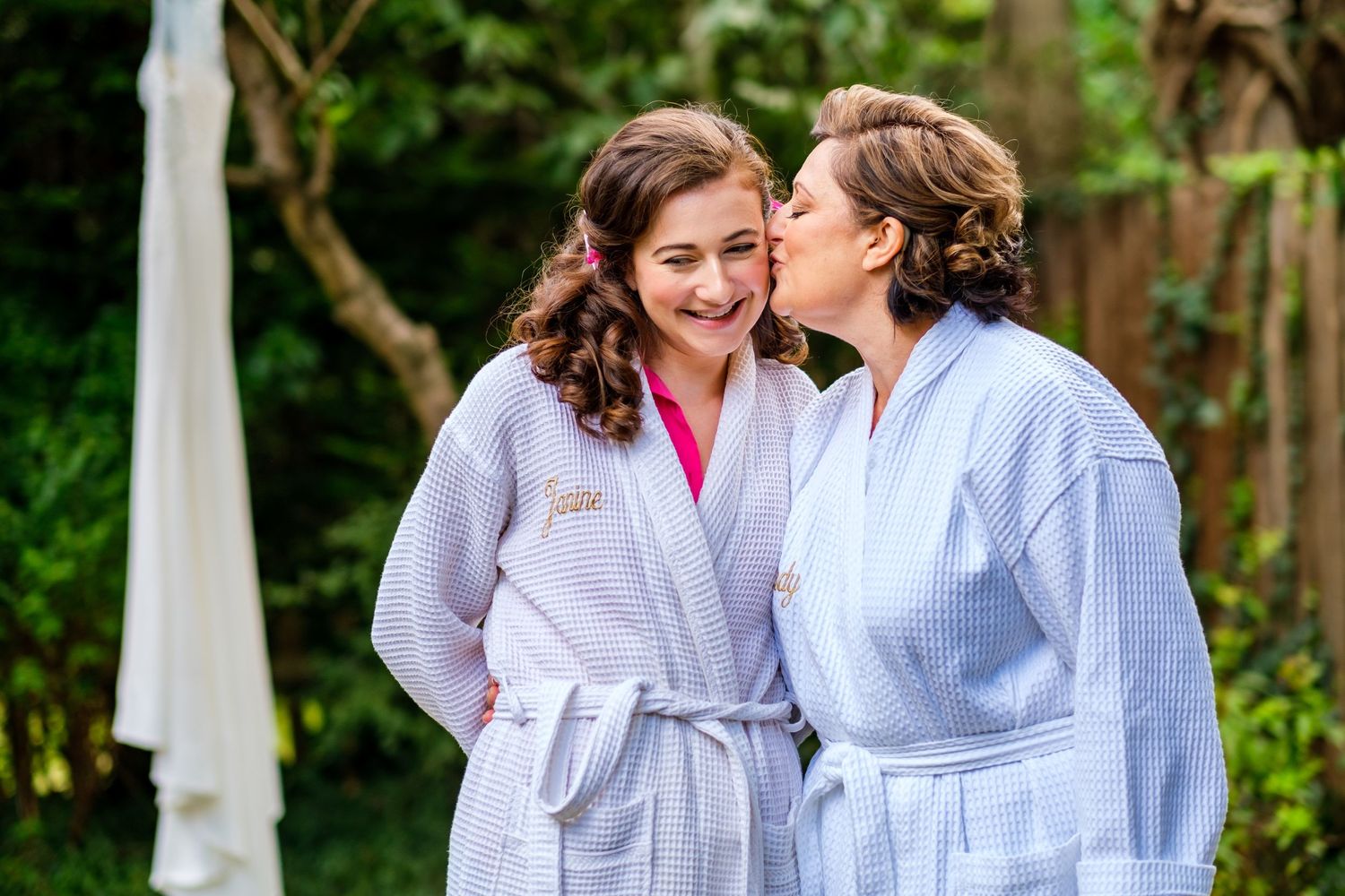 Two people in matching white robes share an intimate moment in a garden setting.
