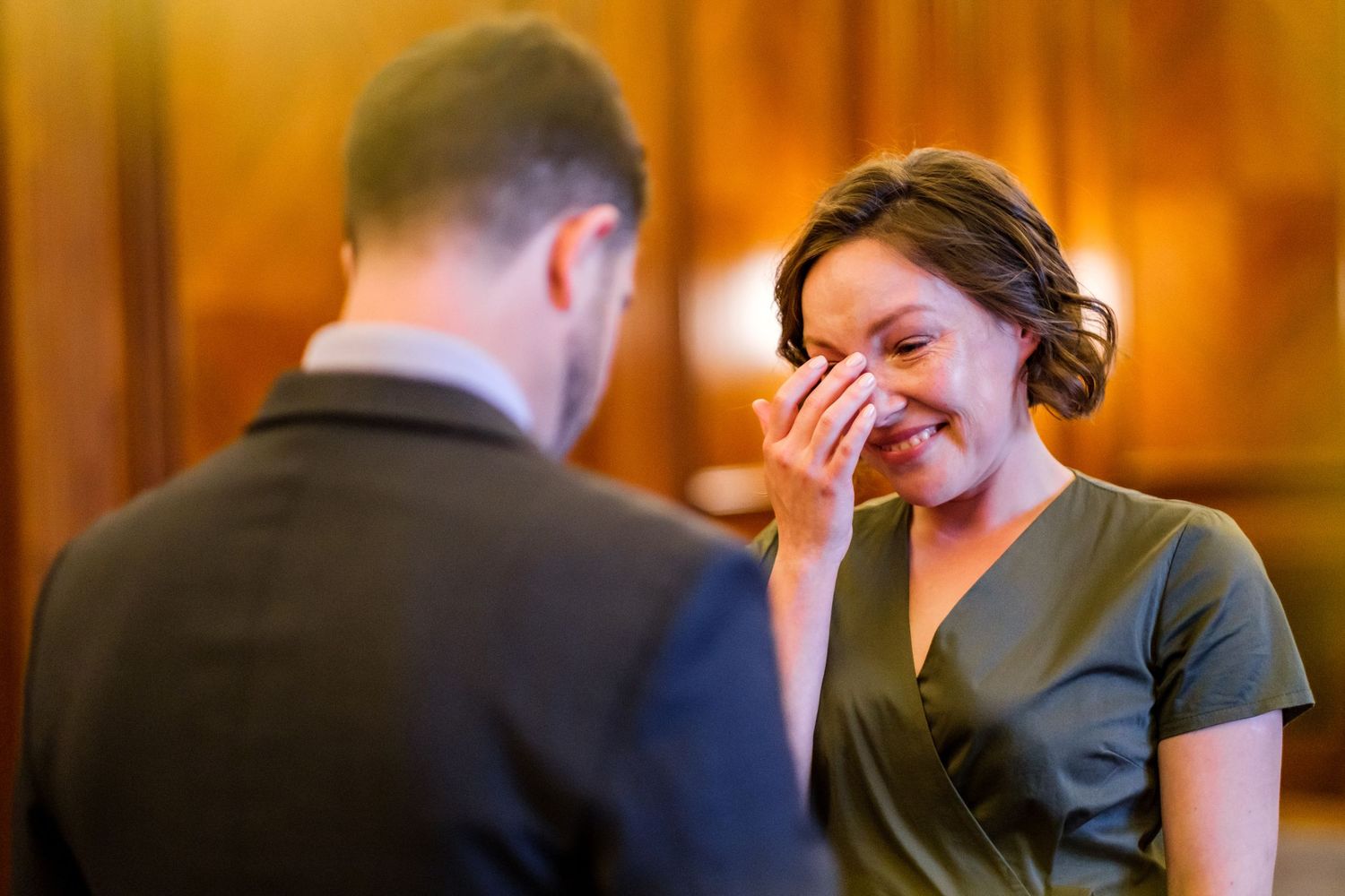 An emotional moment captured during a wedding ceremony in a warmly lit room with wooden paneling.