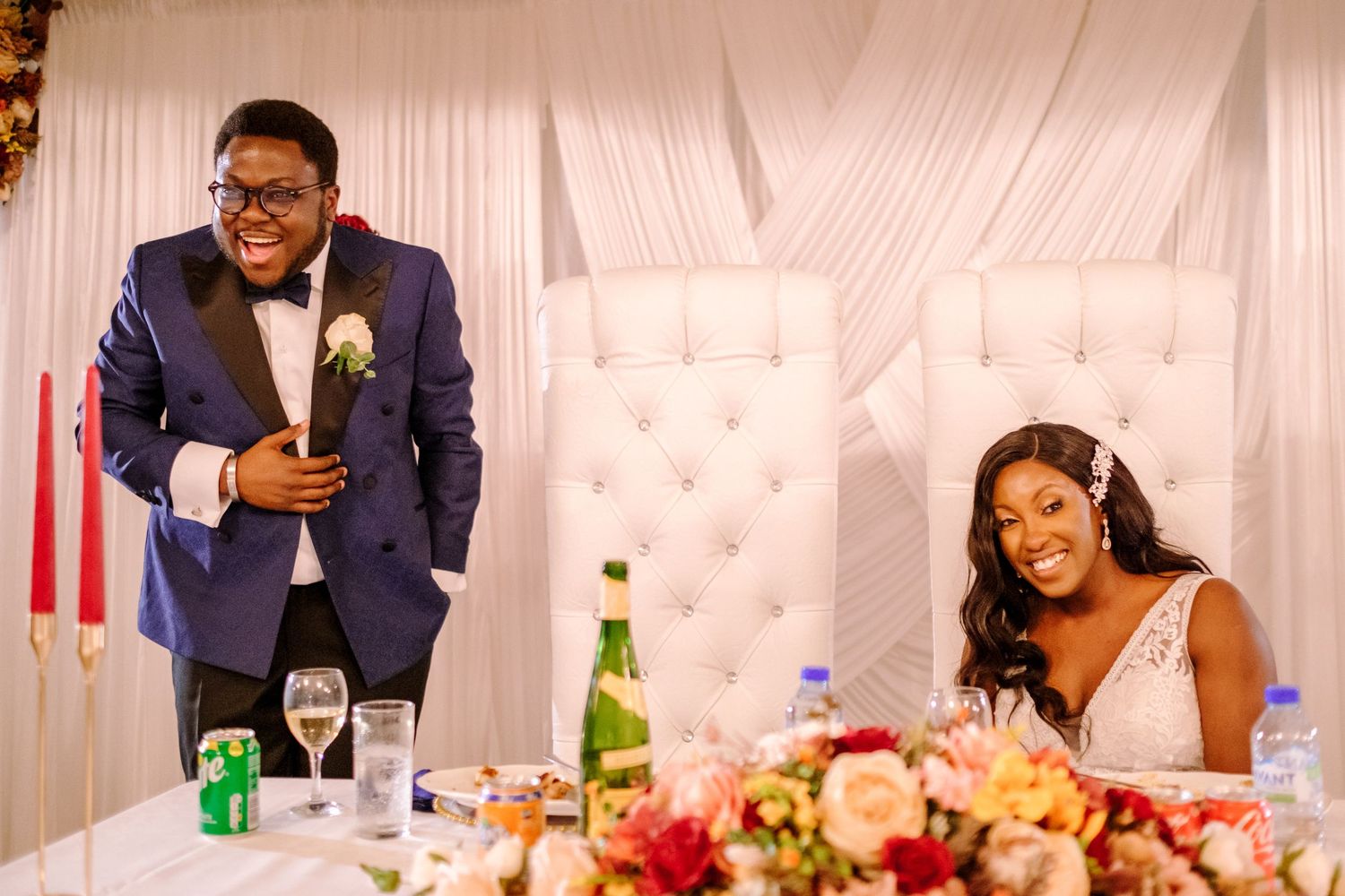 Elegant wedding reception setup with white draping and guests seated at decorated tables.