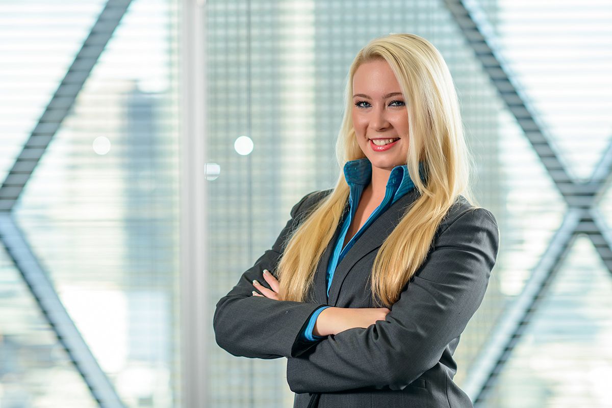 Professional women in business attire smiling in a bright corporate office setting with glass windows.