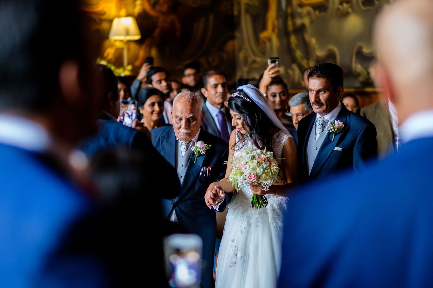 Wedding ceremony processional in an ornate ballroom with warm lighting.