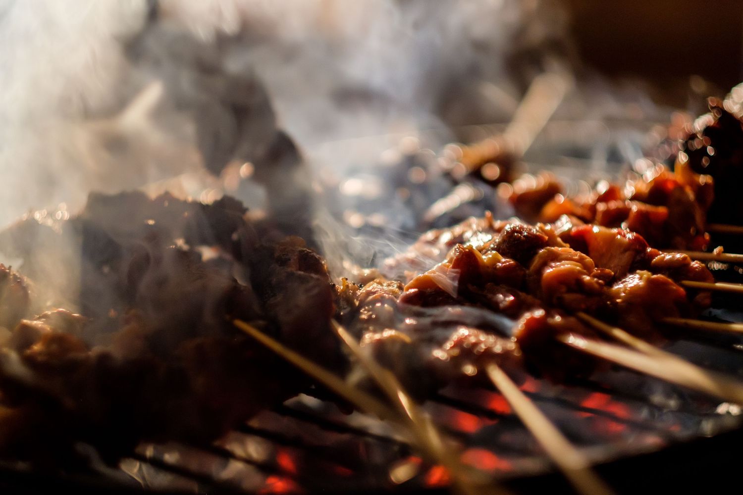Close-up of meat grilling on barbecue with smoke and flames.