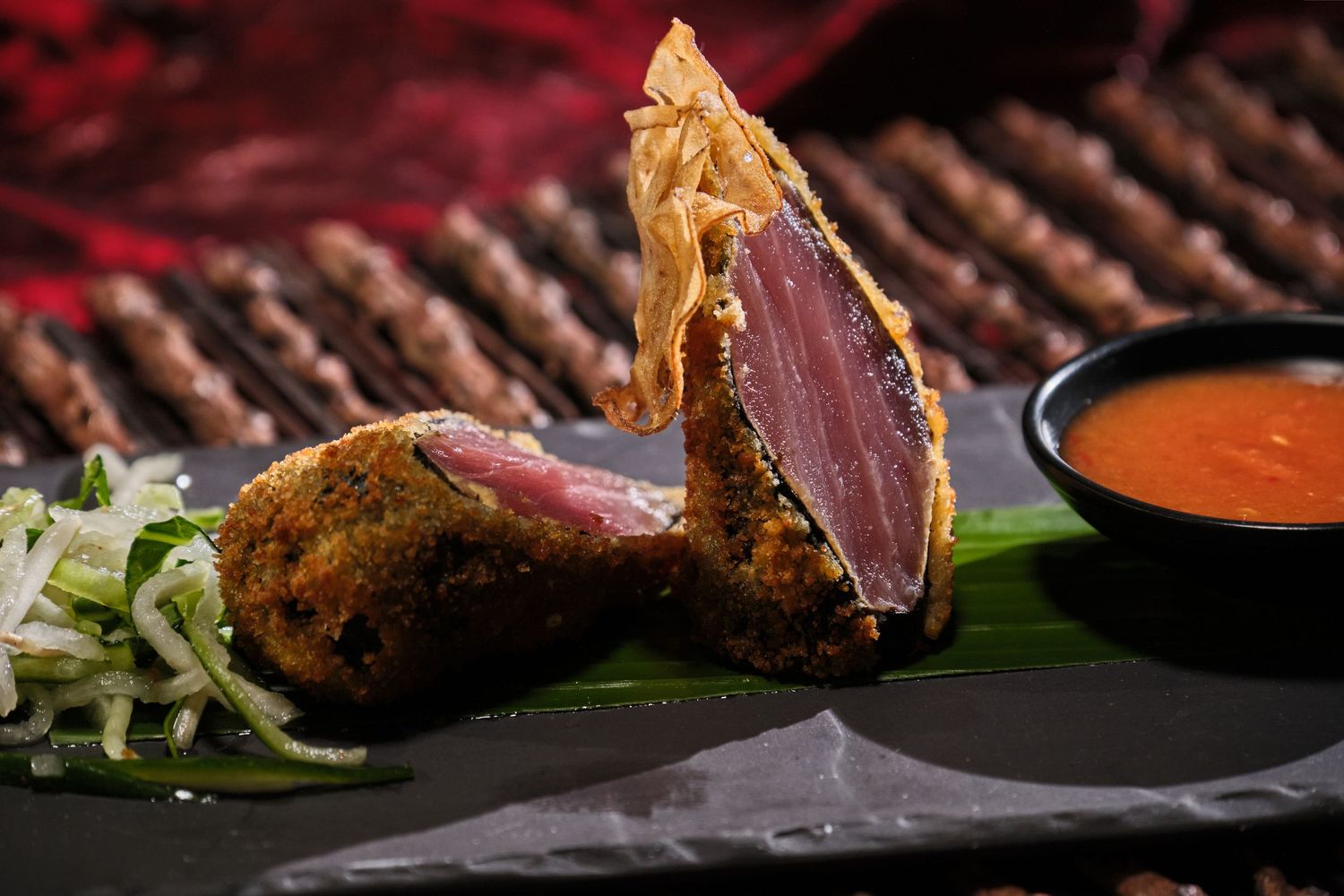 Crispy seared tuna steak with herb crust, served with julienned cucumber, dipping sauce on dark slate plate.